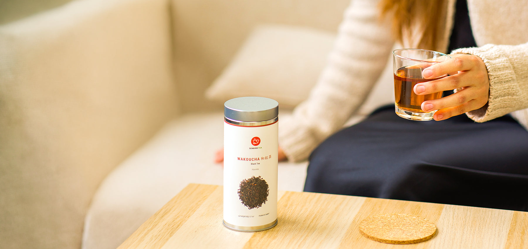 Senbird Wakoucha tea tin beside a person holding a glass of Japanese black tea